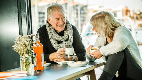 Eldre par drikker kaffe og smiler til hverandre