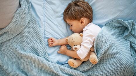 Liten gutt sover trygt i sengen med en bamse