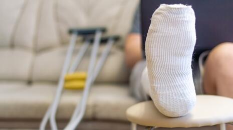 Nærbilde av bandasjert fot med krykker i bakgrunnen