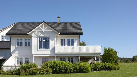 Stort, hvitt hus med husforsikring fra Tryg, omringet av grønn og frodig hage