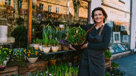 Handel og service. En dame står utenfor blomsterbutikken sin og holder en blomsterbukett