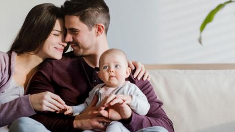 Mor, far og baby sitter i sofaen i leiligheten sin