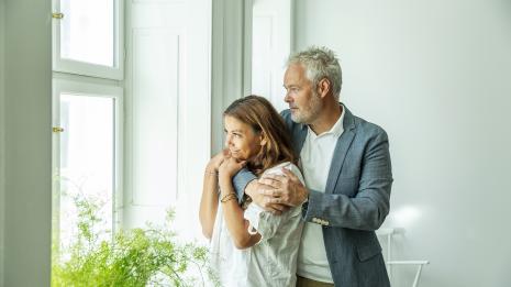 Ektepar holder rundt hverandre og ser ut vinduet. Foto