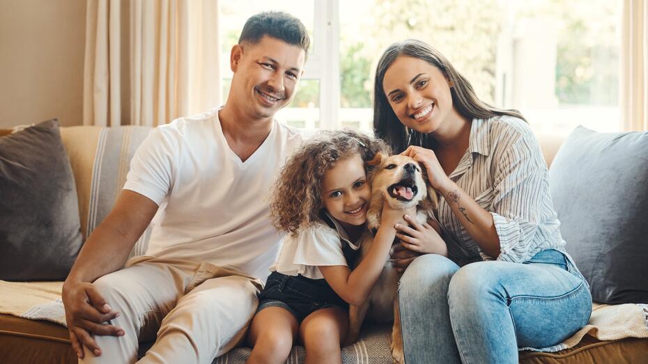 Mor, far, datter og hund sitter på sofaen og smiler