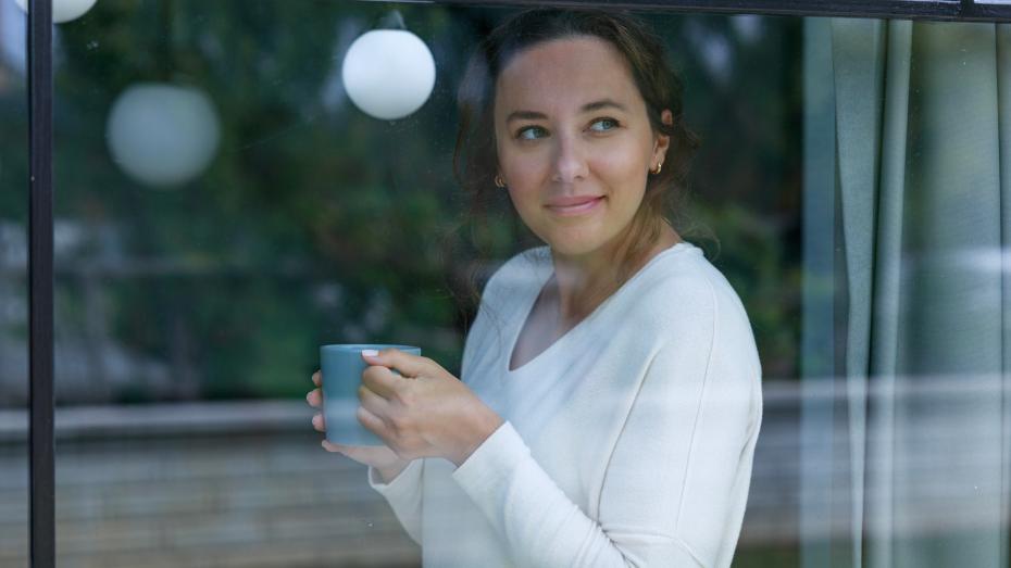 Dame holder kopp og ser ut vinduet. Foto