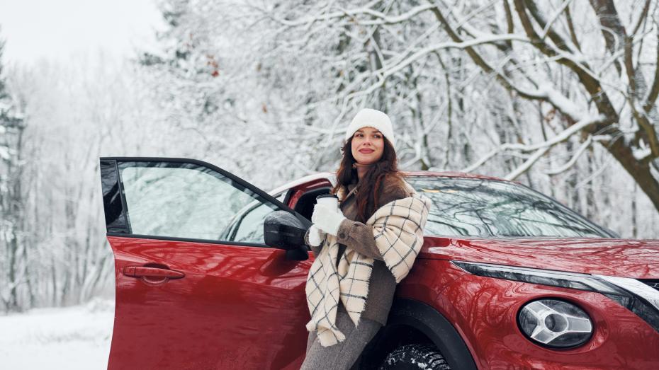 Dame drikker kaffe foran rød bil