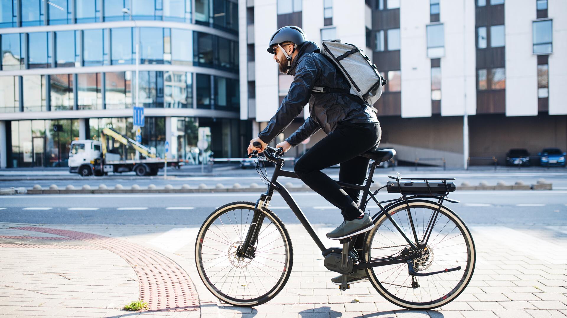  Mann med hjelm og ryggsekk sykler i urbane omgivelser over et gangfelt