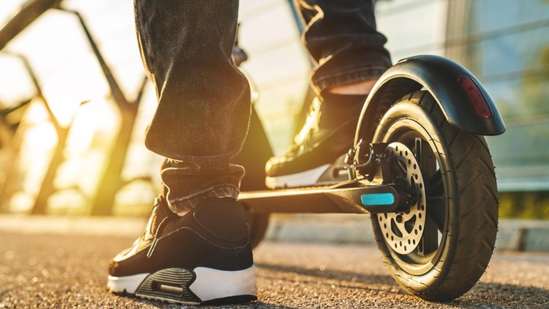 Person som står på en elektrisk sparkesykkel på en solrik dag