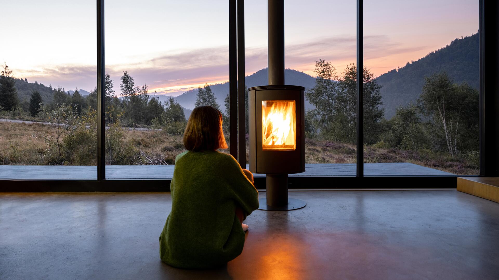 Kvinne sitter foran peis i huset sitt
