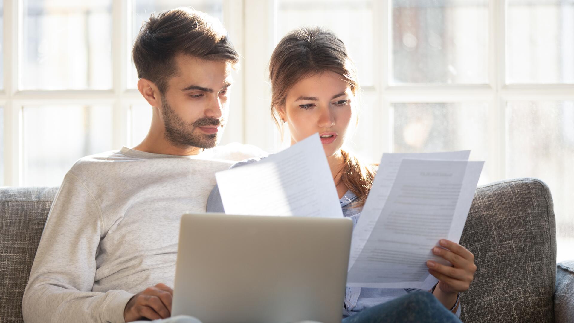 Ungt par som sitter i sofaen med laptop og gjennomgår viktige dokumenter sammen