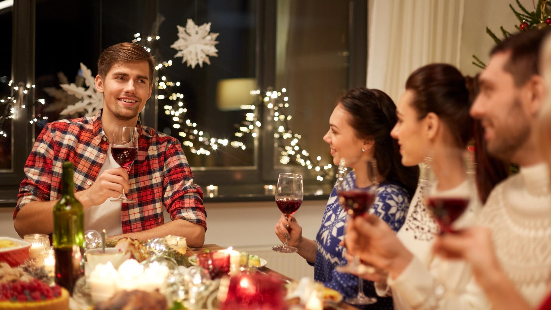 Folk som skåler med rødvinsglass, rundt et julebord