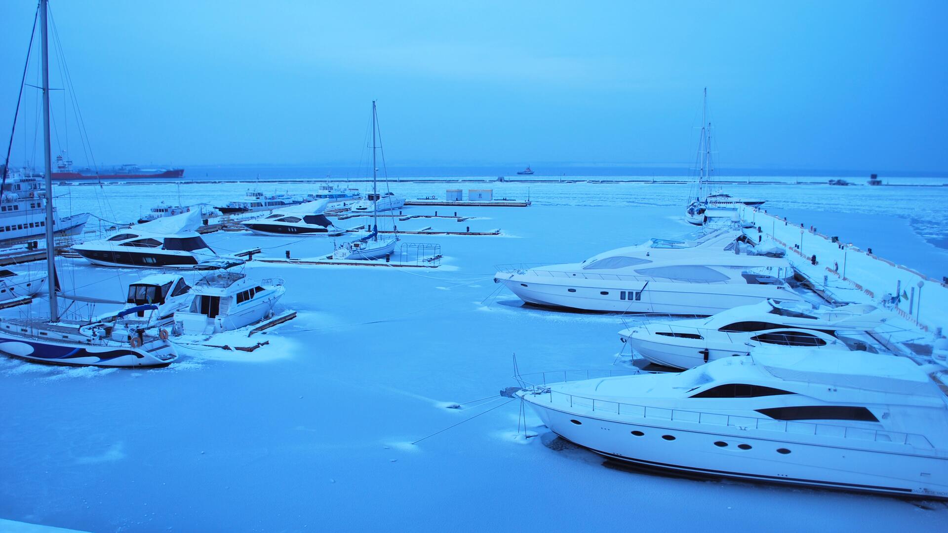 Båter fortøyd i småbåthavn om vinteren, omgitt av is og snø.