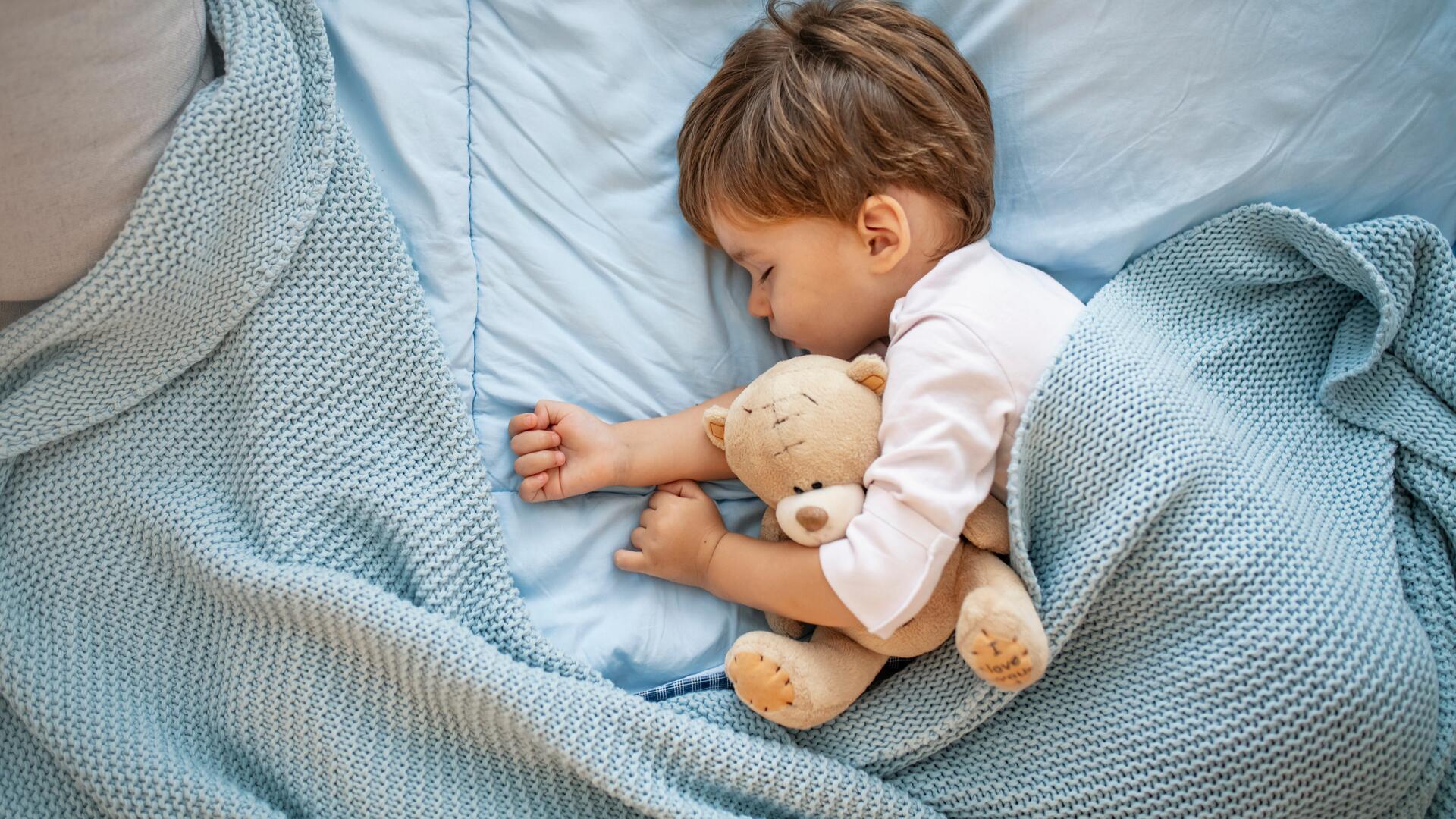 Liten gutt sover trygt i sengen med en bamse