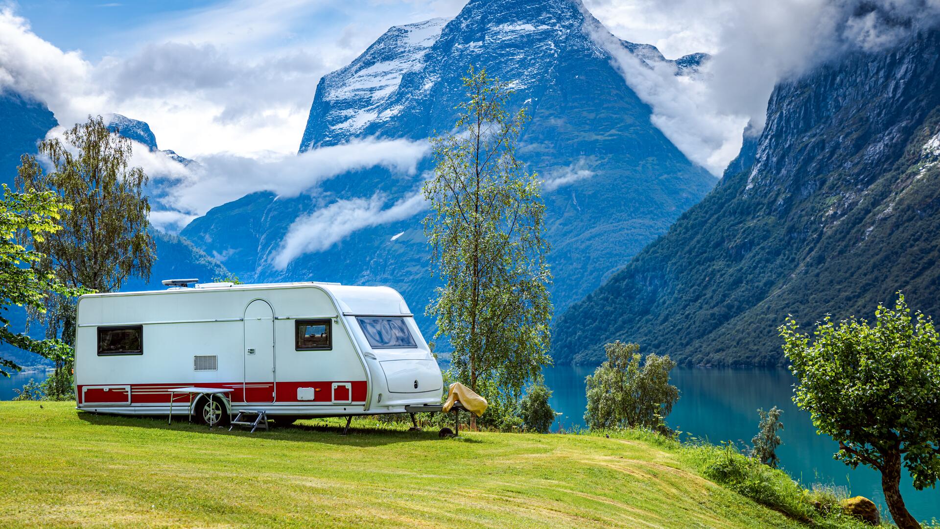 Campingvogn parkert på grønn slette ved fjord og fjell.