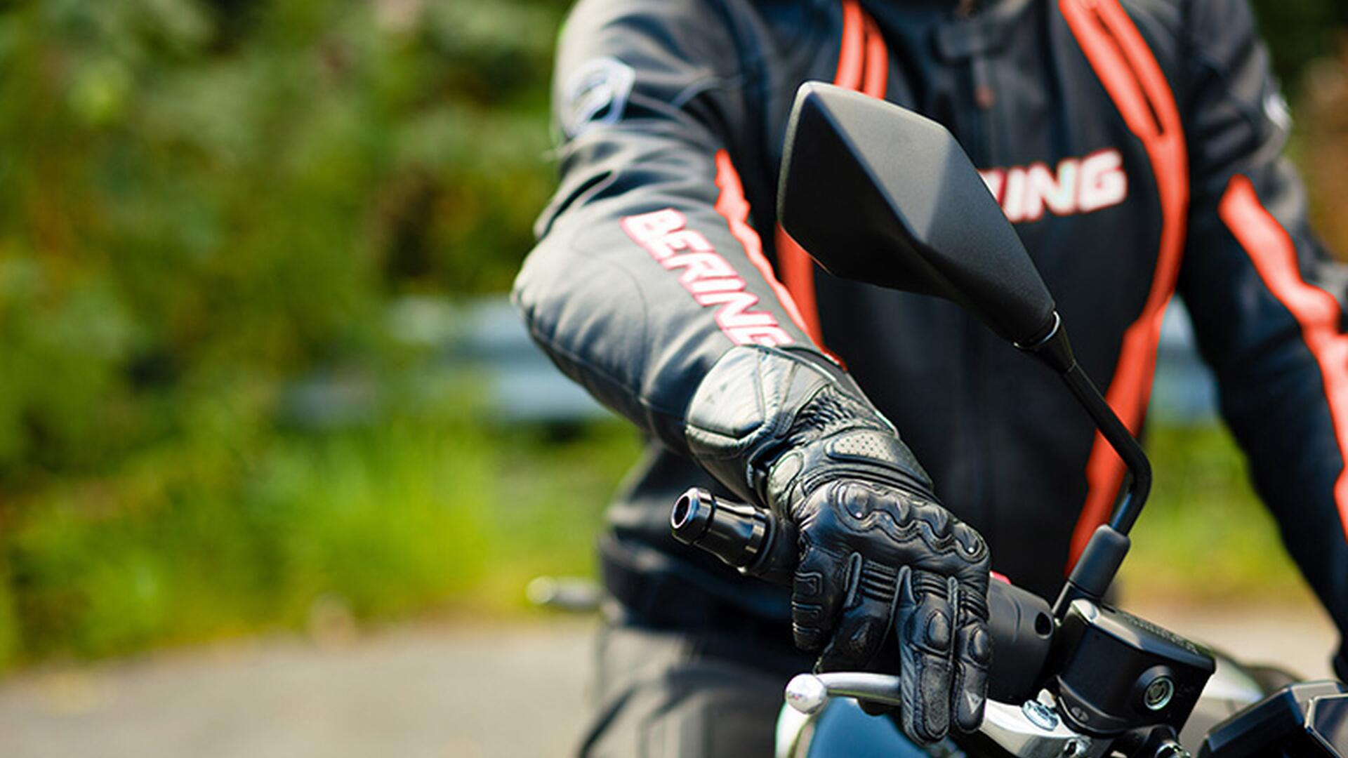 Motorsyklist iført svart og oransj kjøredress sitter på motorsykkelen sin