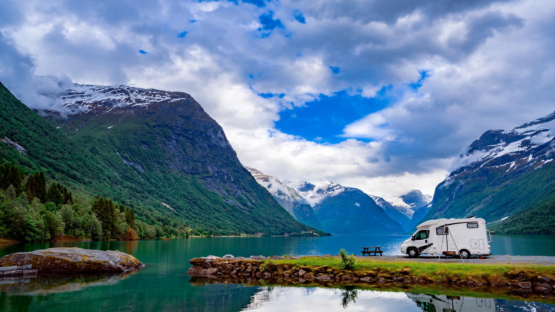 Bobil parkert ved innsjø omgitt av fjell og norsk natur