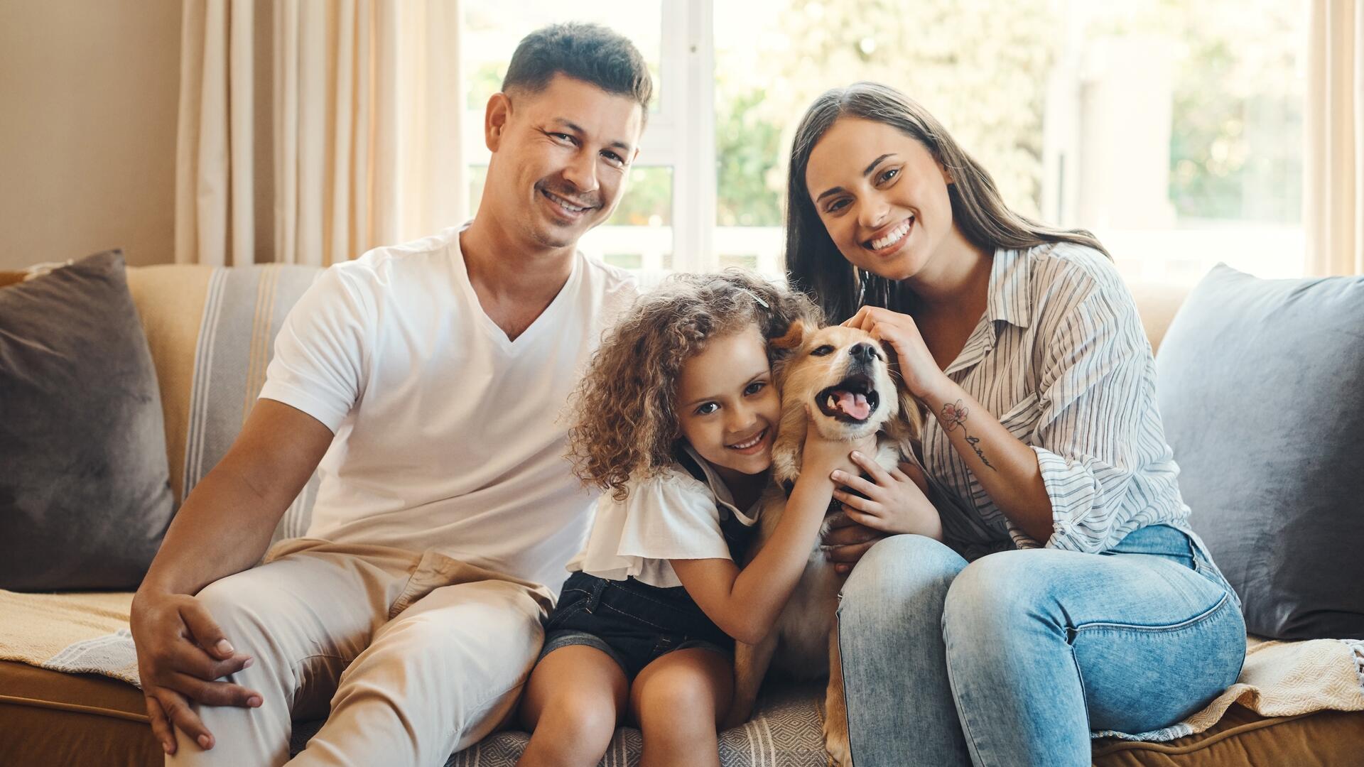 Mor, far, datter og hund sitter på sofaen og smiler