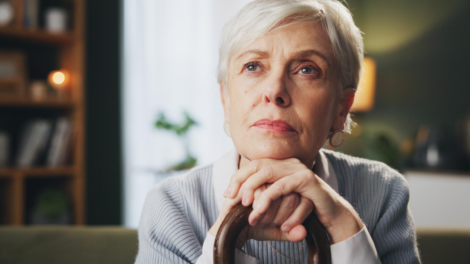Eldre kvinne sitter på sofa og tenker, og ser bekymret ut
