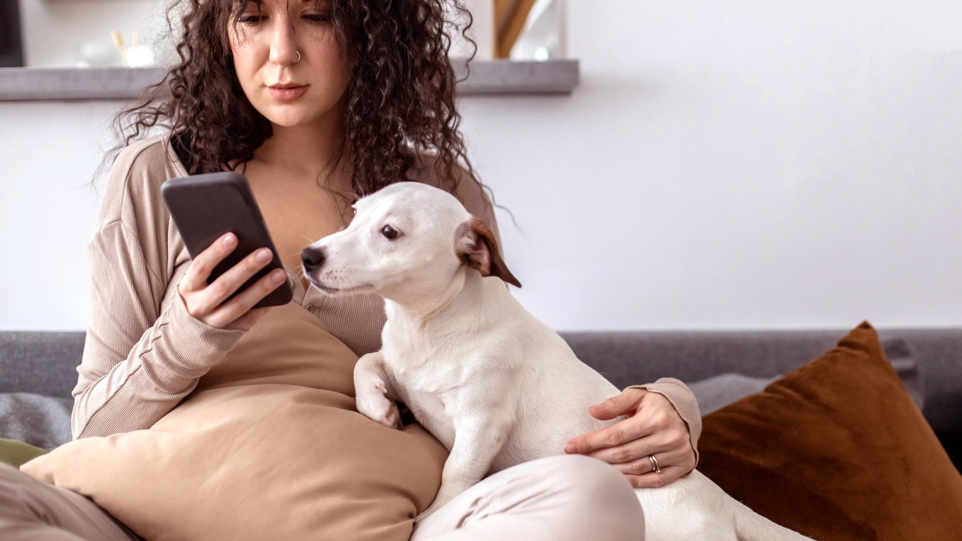 Dame som koser med hunden sin mens hun er på telefonen
