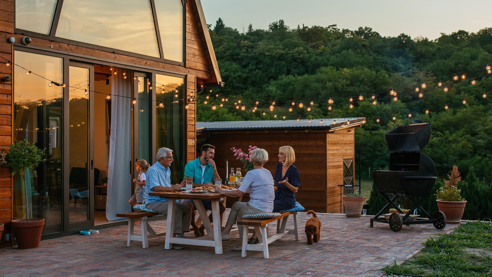Familie nyter middag ute på terrasse, omgitt av lyslenker og grønne omgivelser.