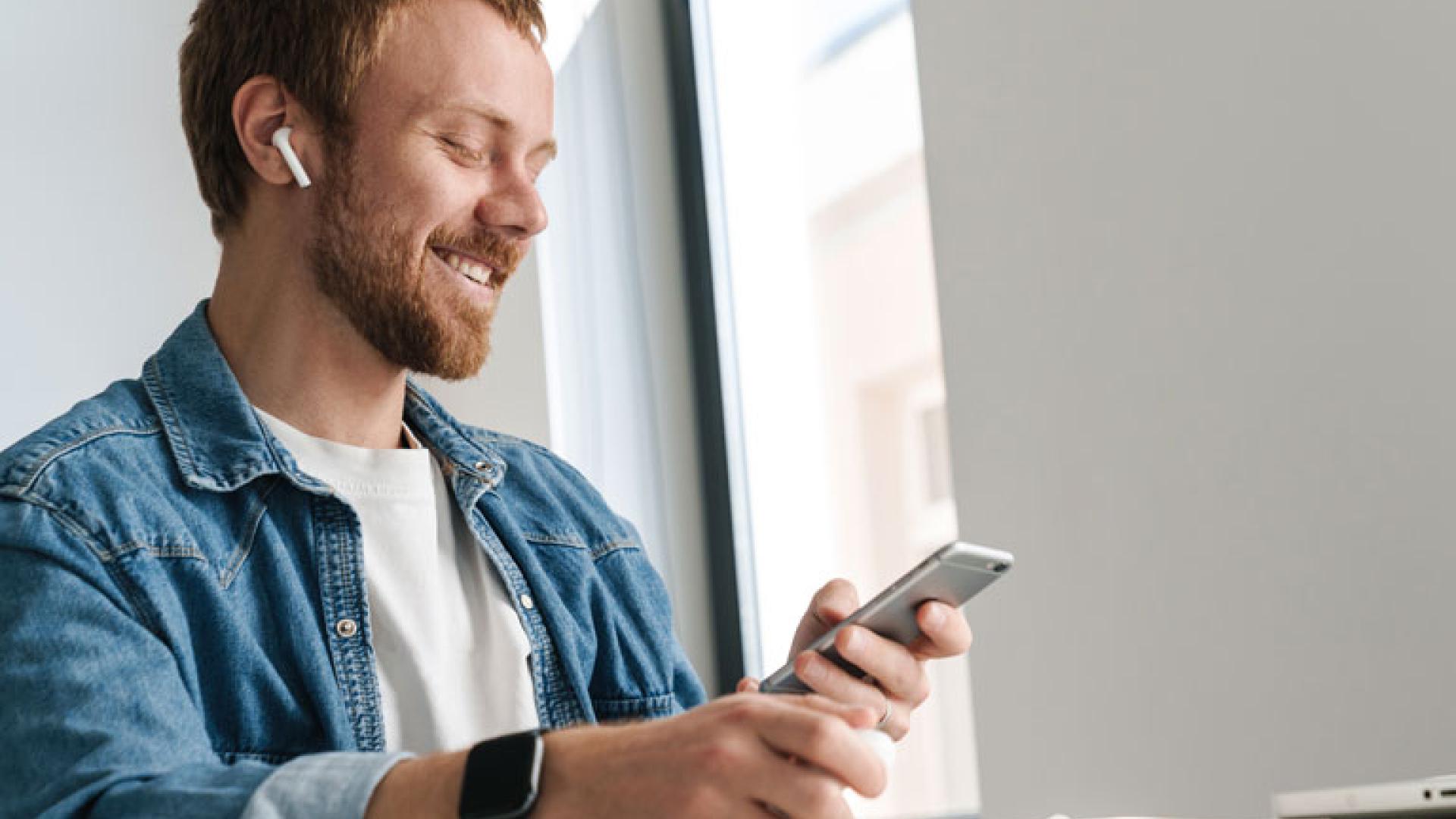 Mann som ser smilende ned på telefonen sin