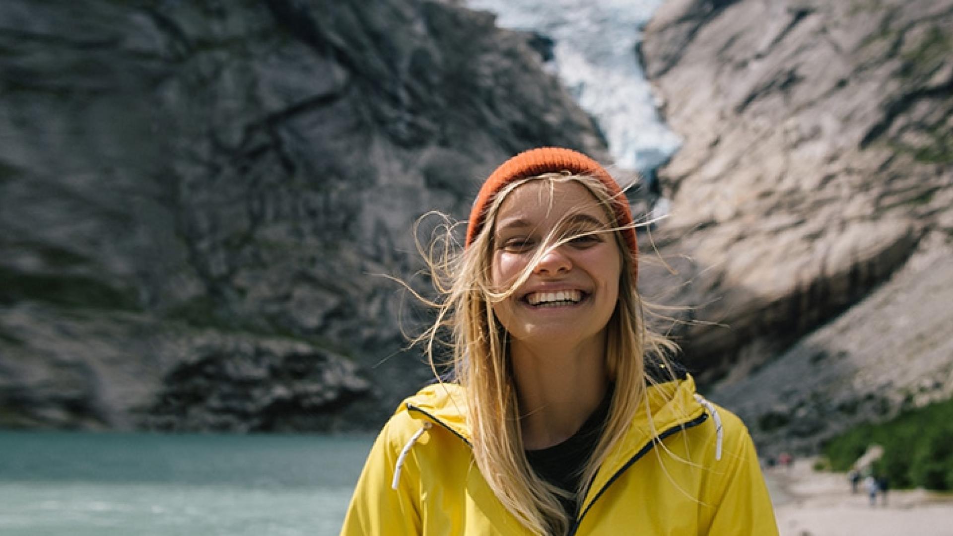 Kvinne smiler foran fjell og innsjø i naturen