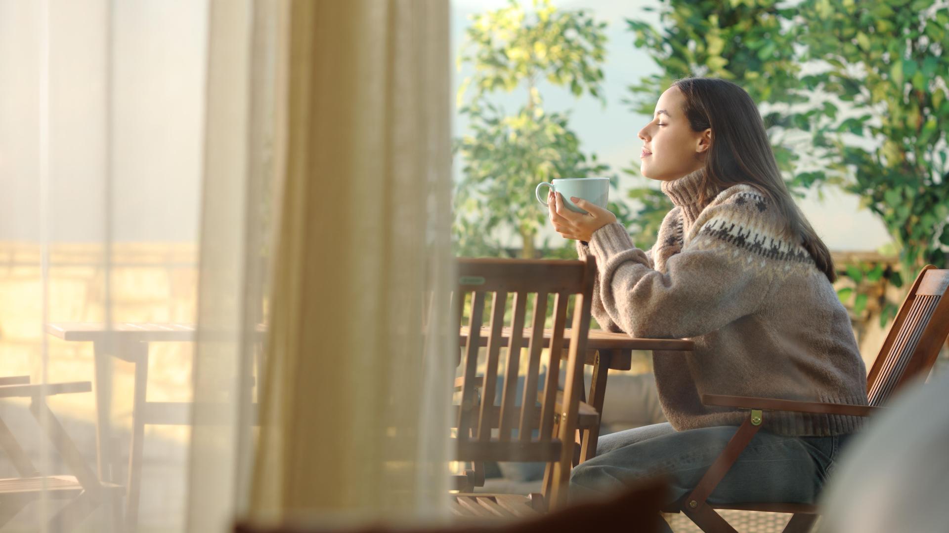 Dame med kaffekopp sitter ute i finvaeret. Foto
