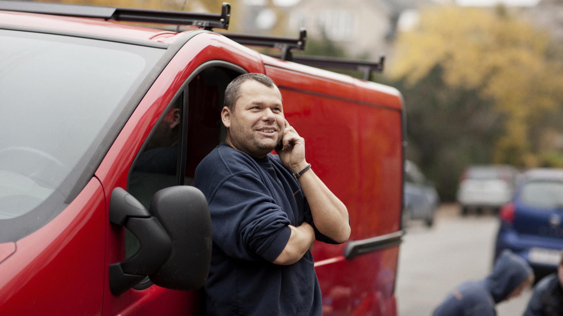 En mannlig håndverker står utenfor firmabilen sin og snakker i telefonen. Foto