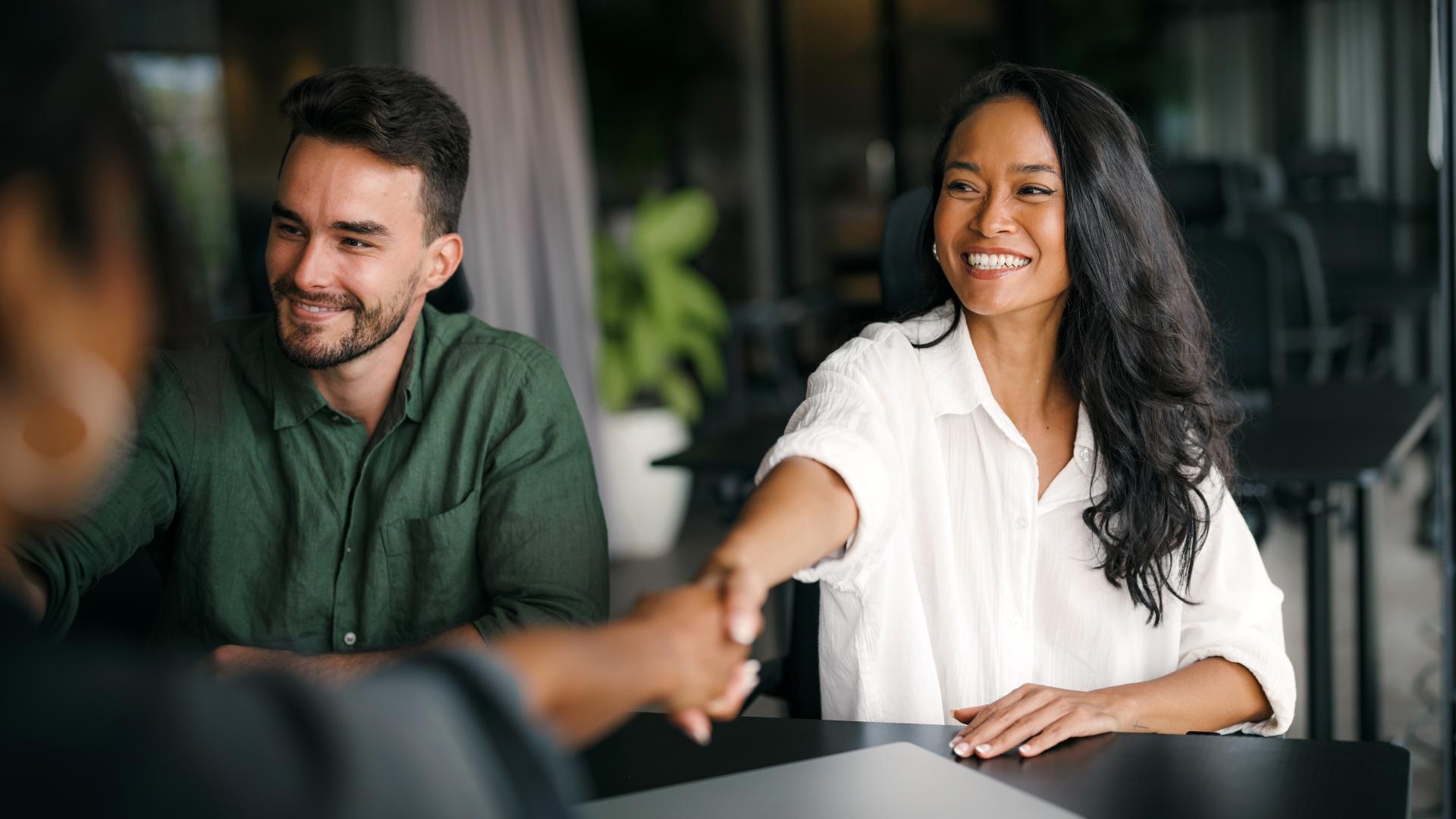 En mann og en dame handhilser med en tredje person. Foto