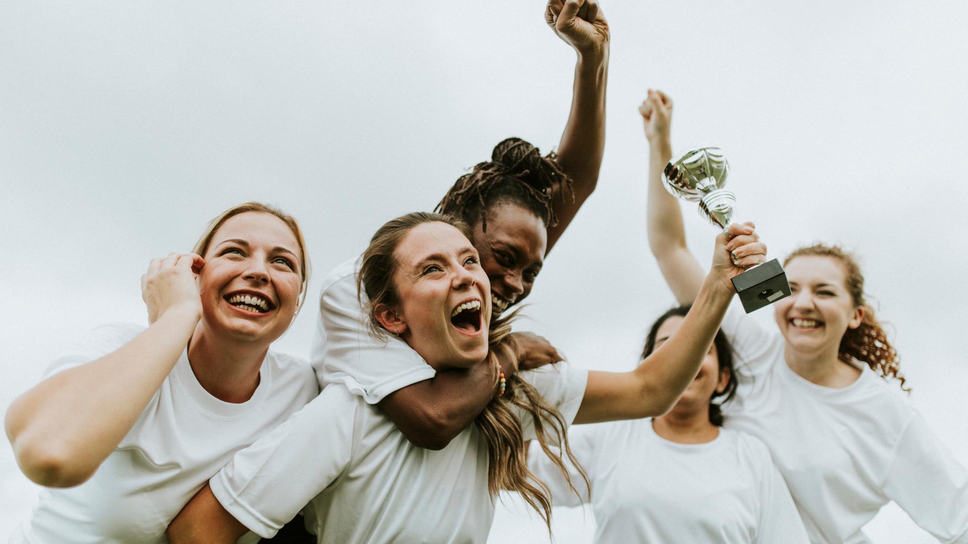 Kvinnelige lagspillere som feirer og lofter en pokal. Foto