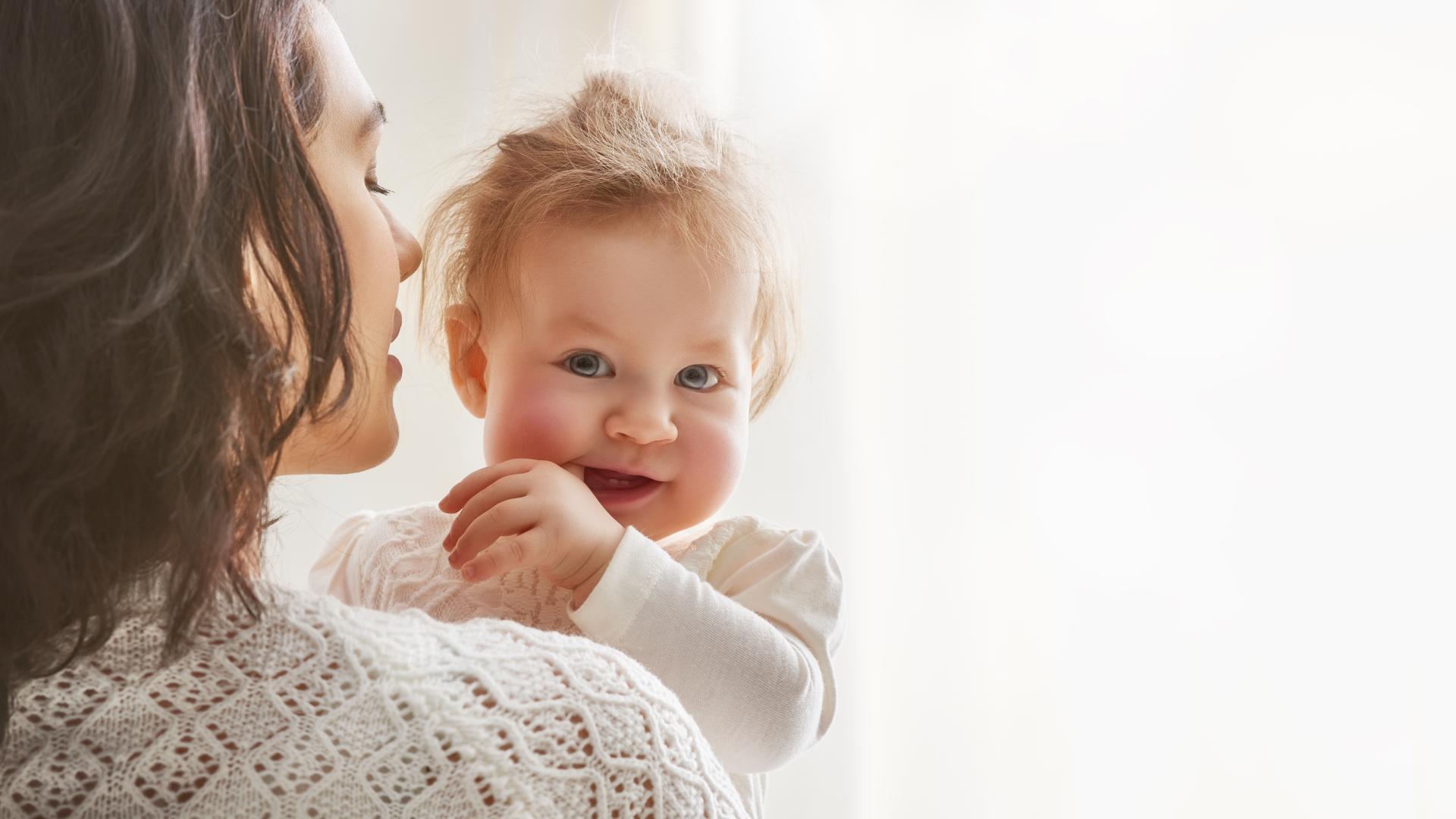 Smilende baby i armene til moren sin