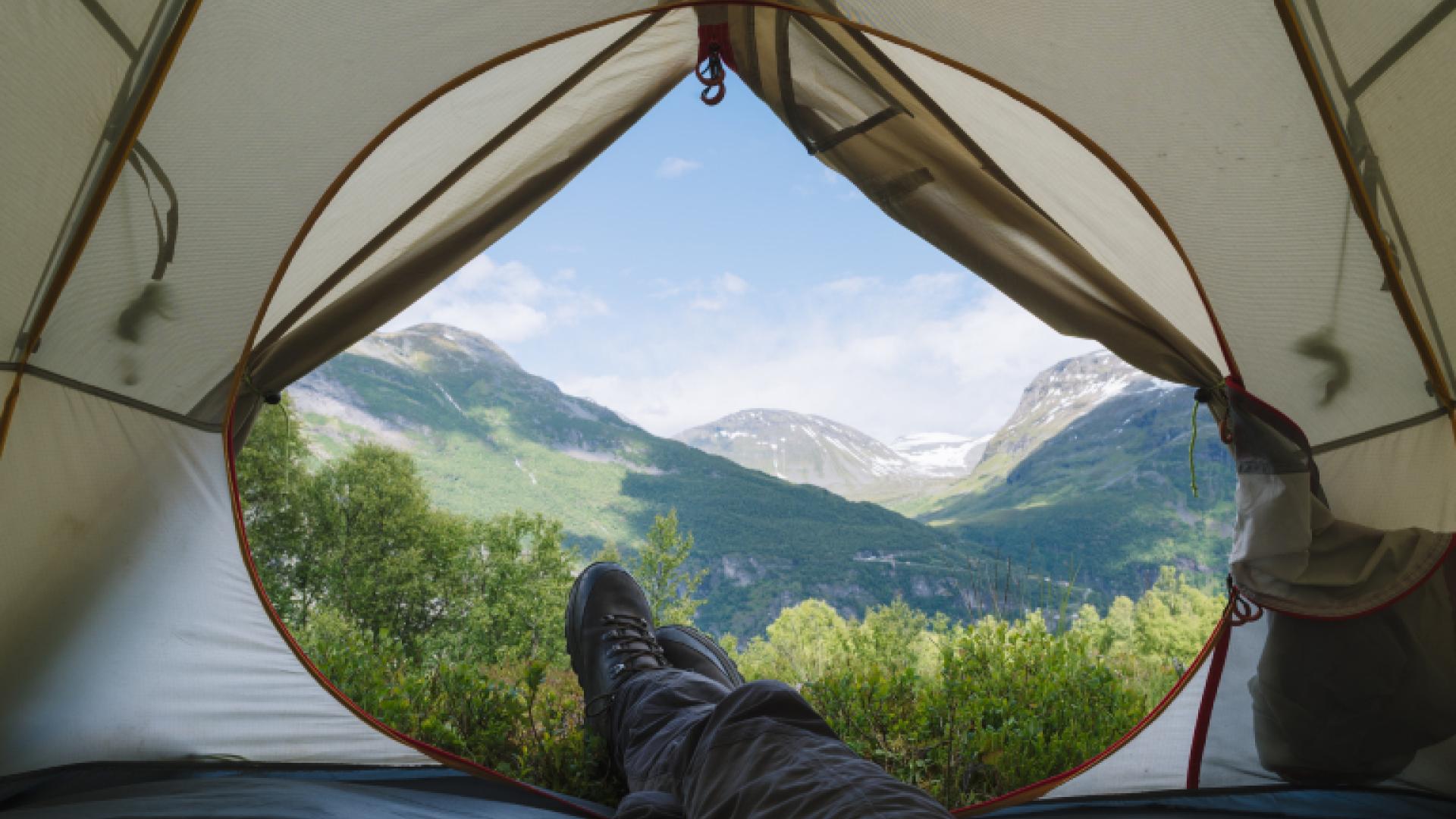 Mann som ligger i teltet sitt med fin utsikt over fjellene 