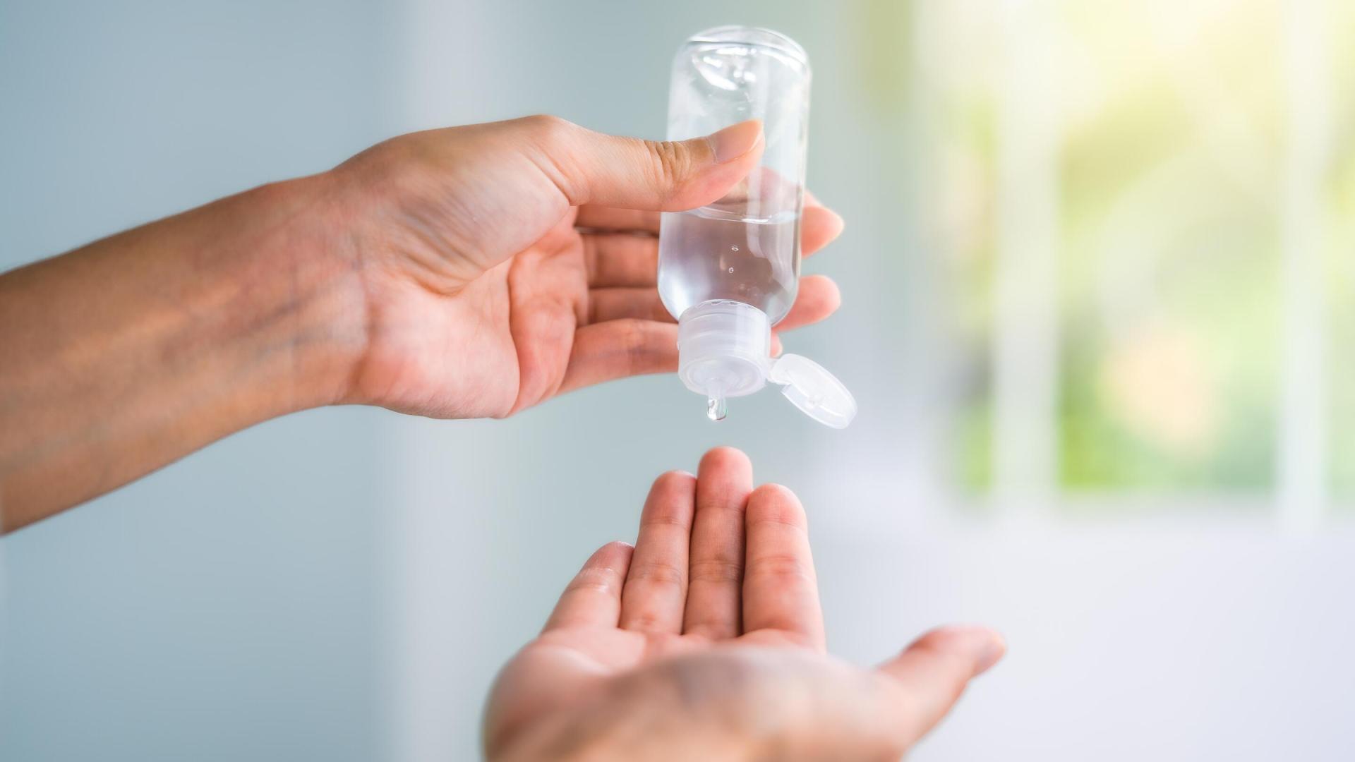 Person klemmer hånddesinfeksjon ut av en liten flaske og ned i hånden, med fokus på hygiene og smittevern.