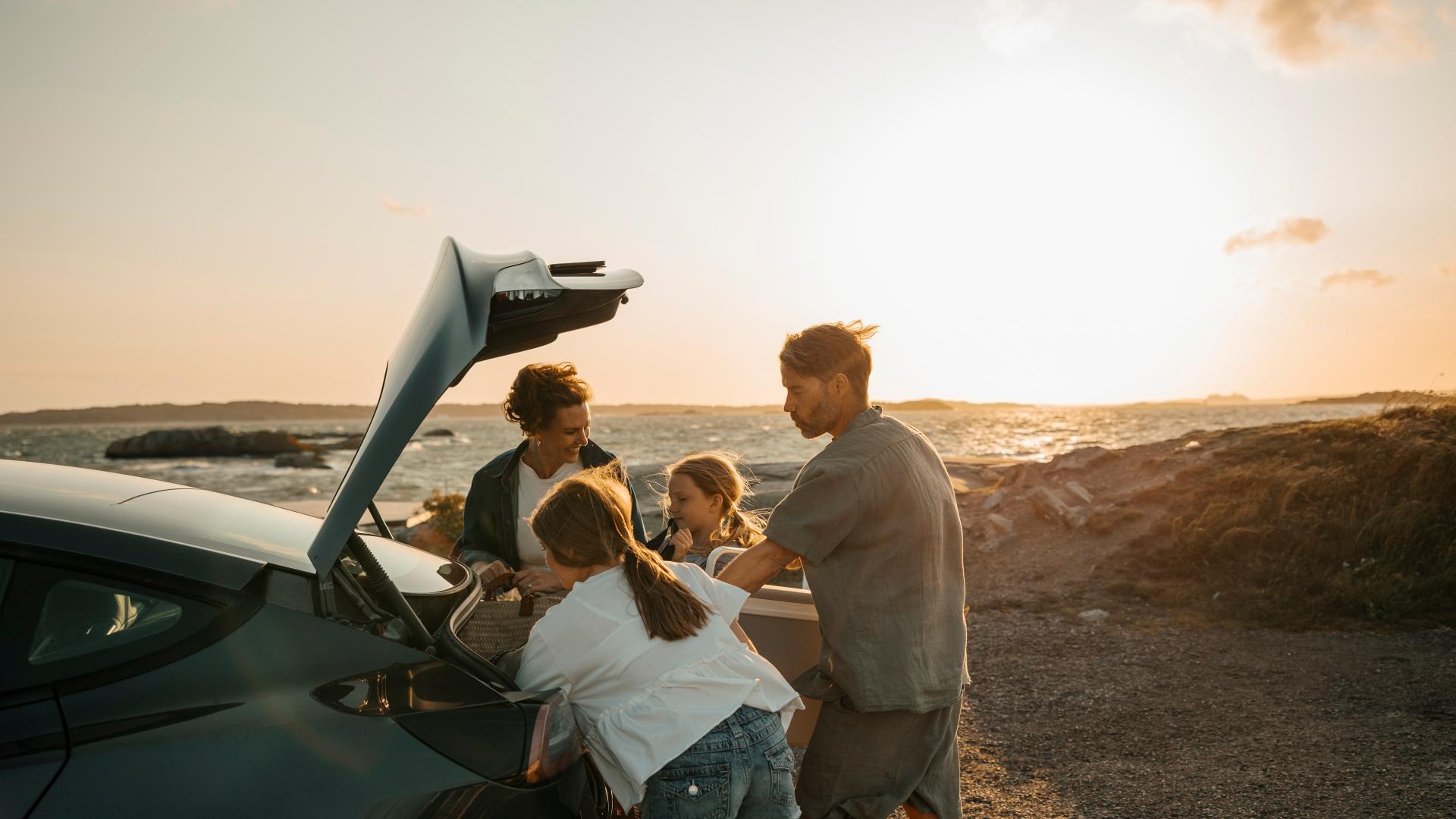 Familie som pakker ut av leiebilen på stranden 