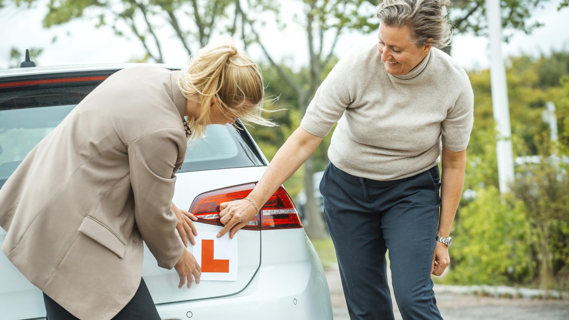 Mor og datter som setter på "L" på bilen før de skal øvelseskjøre 