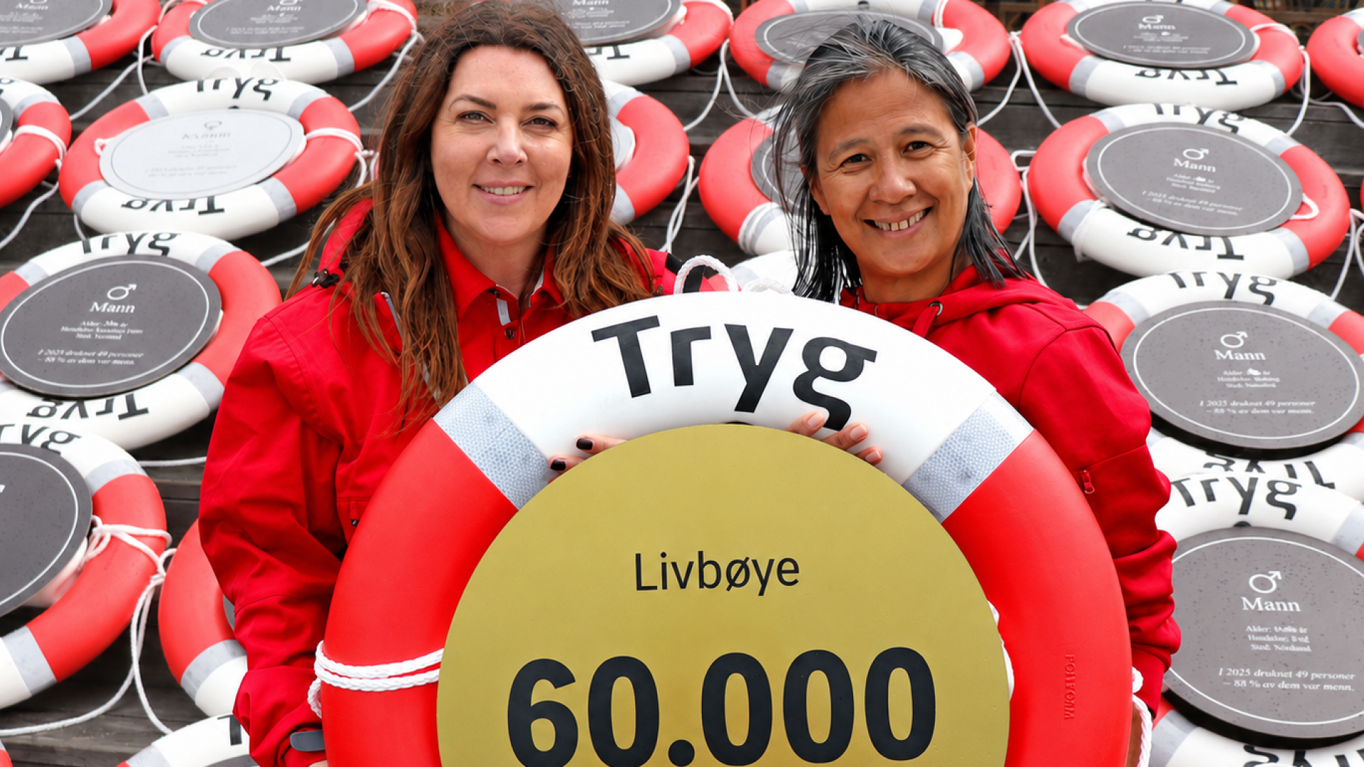 Representanter fra Tryg og Norges Livredningsselskap holder Trygs livbøye nummer 60 000 foran flere røde og hvite livbøyer.