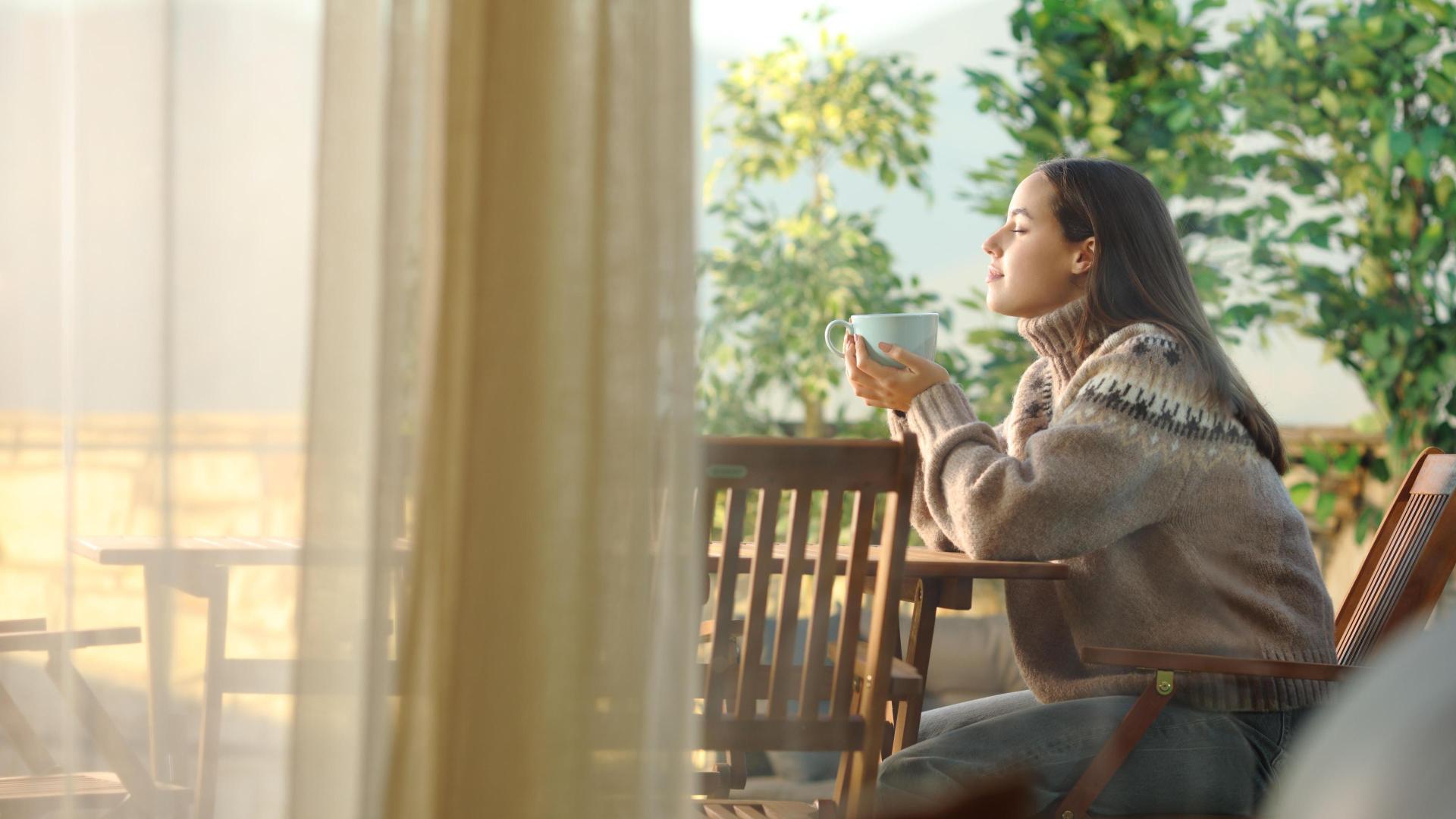 Dame med kaffekopp pa verandaen i finværet
